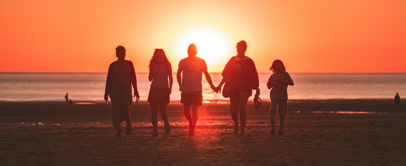 silhouette photo of five person walking on seashore during golden hour