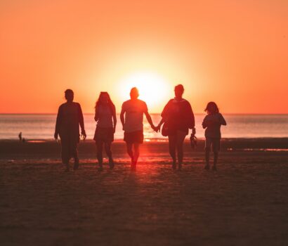 silhouette photo of five person walking on seashore during golden hour