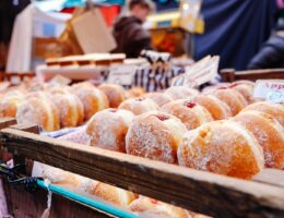 selective focus photography of doughnuts display on brown wooden trays near person wearing black hoodie