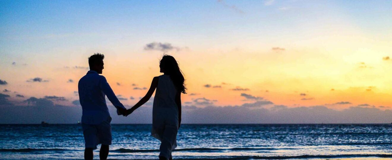 Man and Woman Holding Hands Walking on Seashore during Sunrise